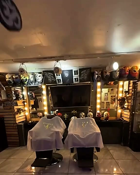 El local de frente: dos sillones con capa blanca, espejos de camerino con focos y la pared de máscaras de lucha libre arriba, sobre piso de loseta brillante